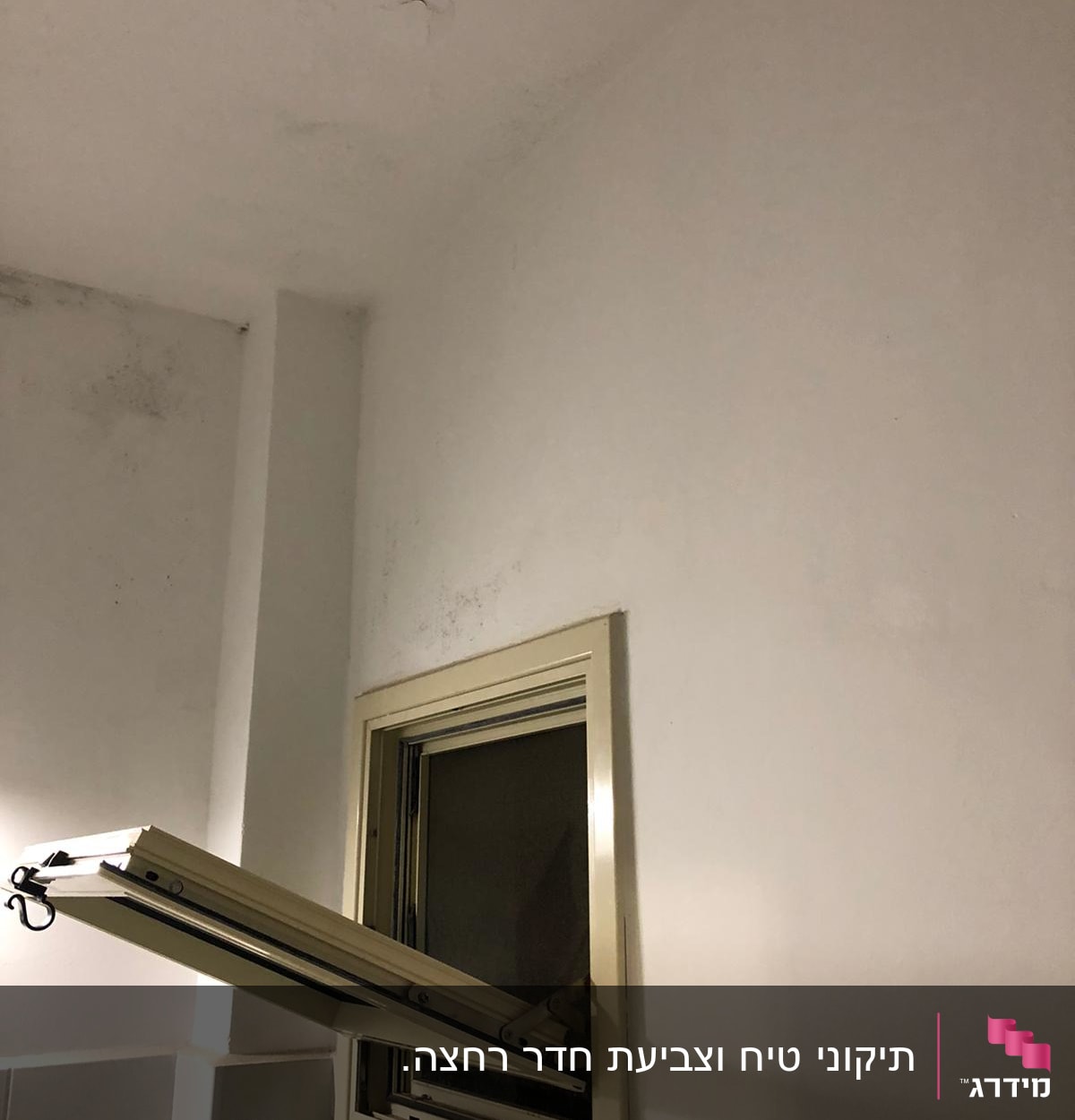קיר לבן עם סימני רטיבות ליד חלון פתוח